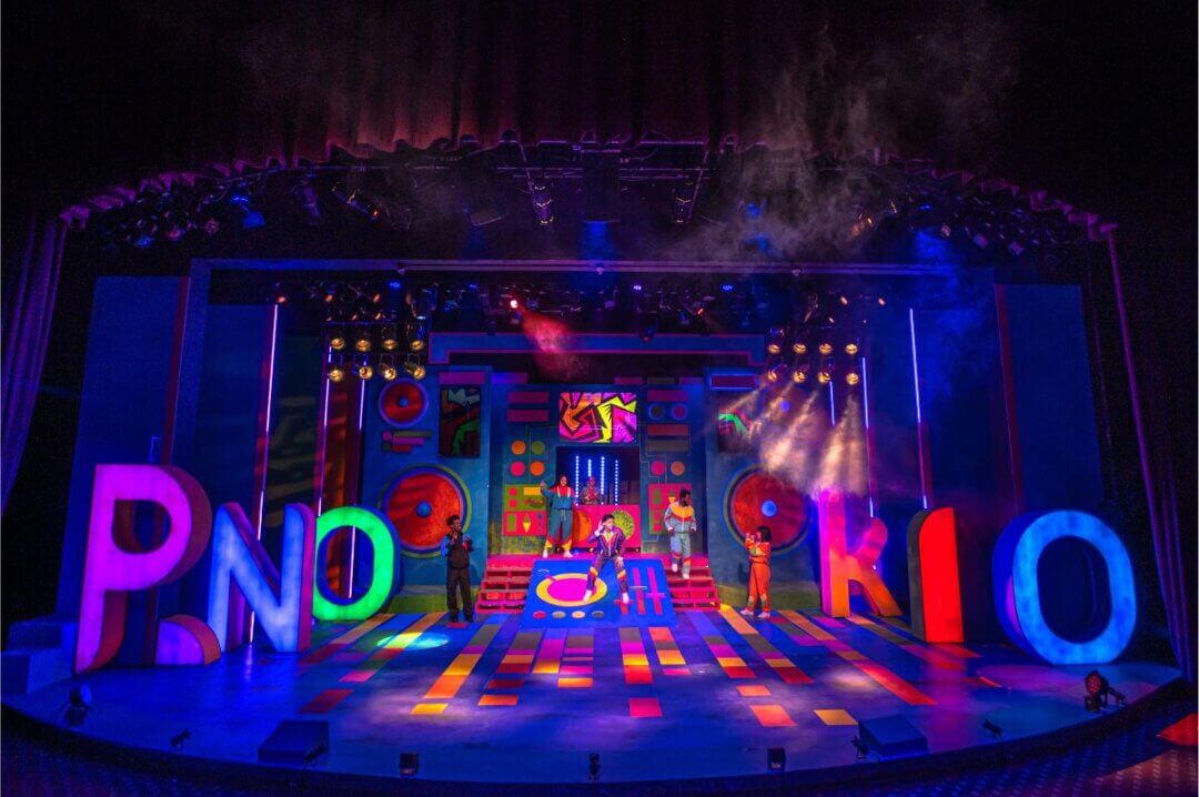 Wide shot of stage with full cast. P.Nokio's name is spelled out in oversized letter lightboxes spanning the stage.